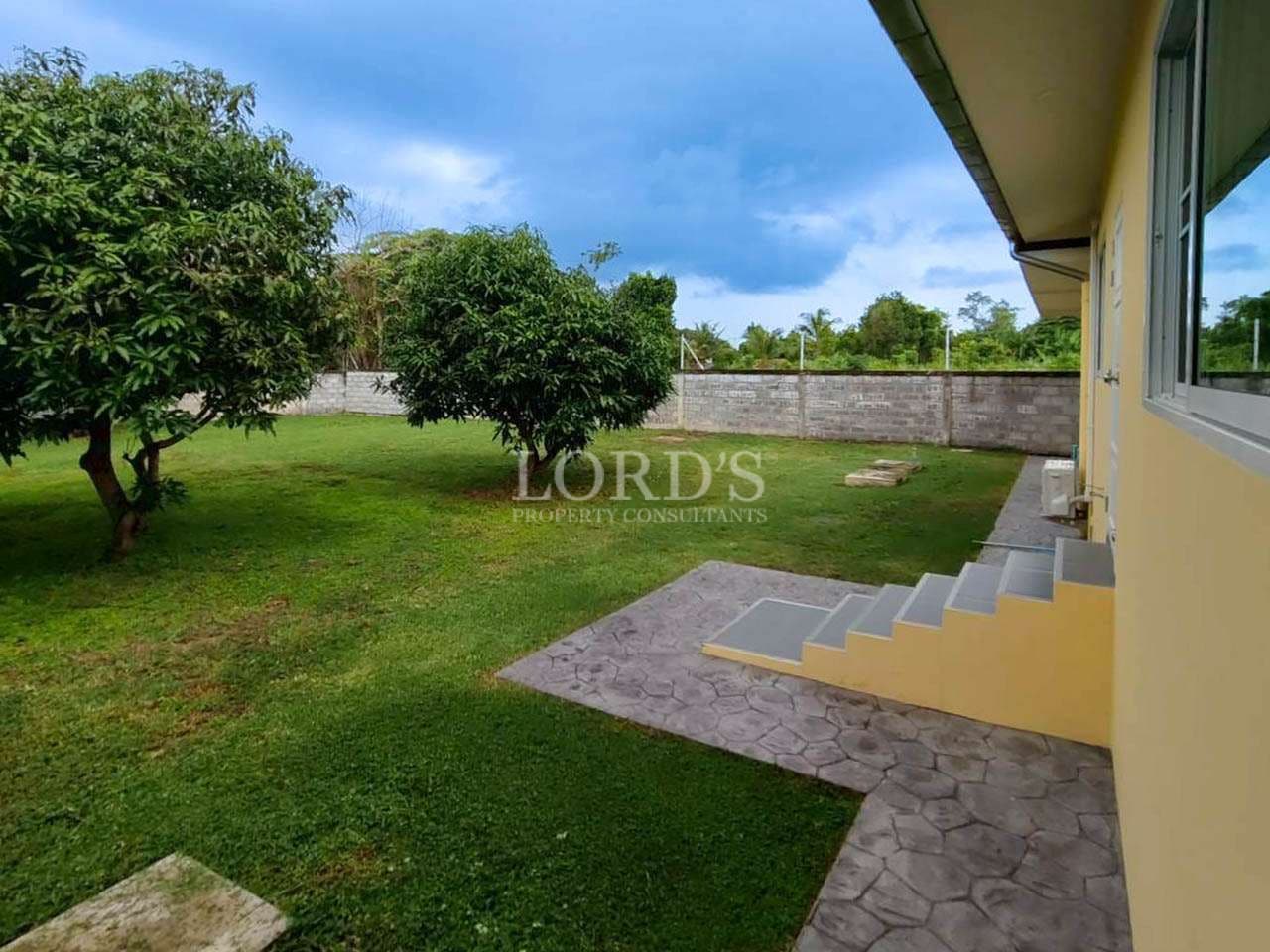 Private garden with mature trees, green lawn, and paved walkway beside the house.