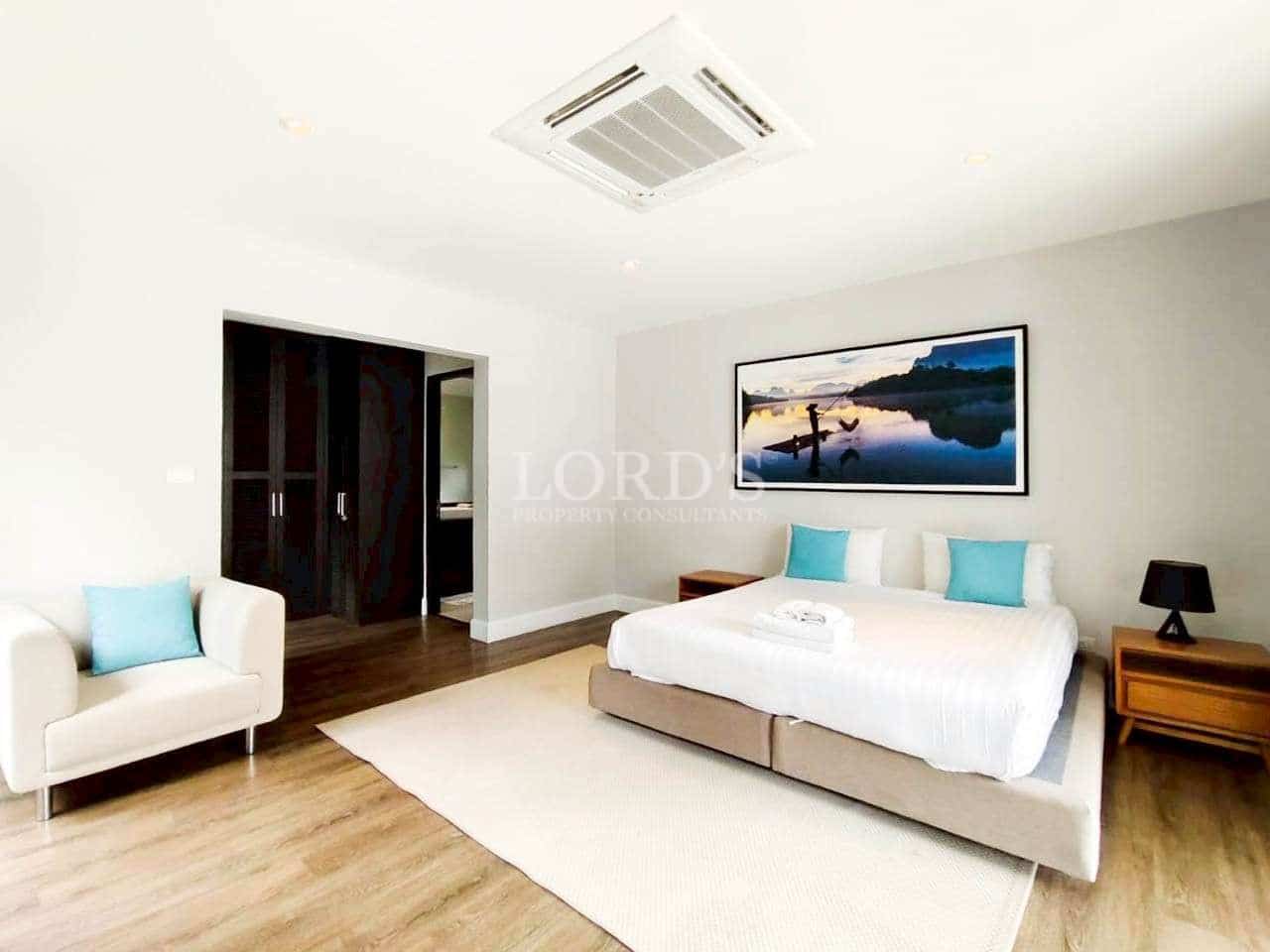 Spacious modern bedroom with king-size bed, wooden flooring, ceiling air conditioner, and minimalist décor