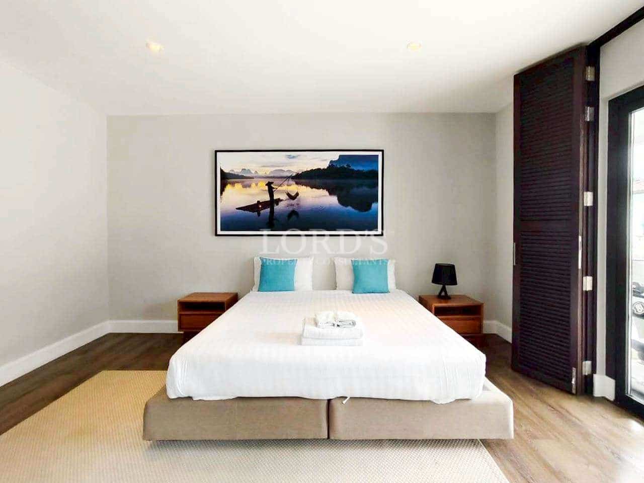 Modern minimalist bedroom with king-size bed, wooden floor, and framed lake landscape artwork
