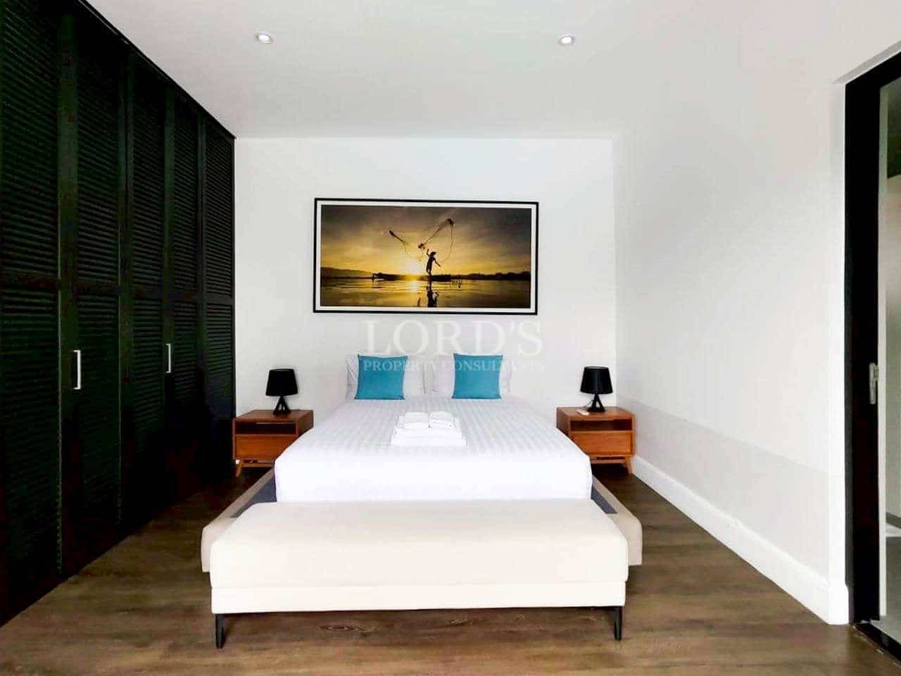 Modern minimalist bedroom with white walls, wooden flooring, black wardrobe, and framed wall art above the bed