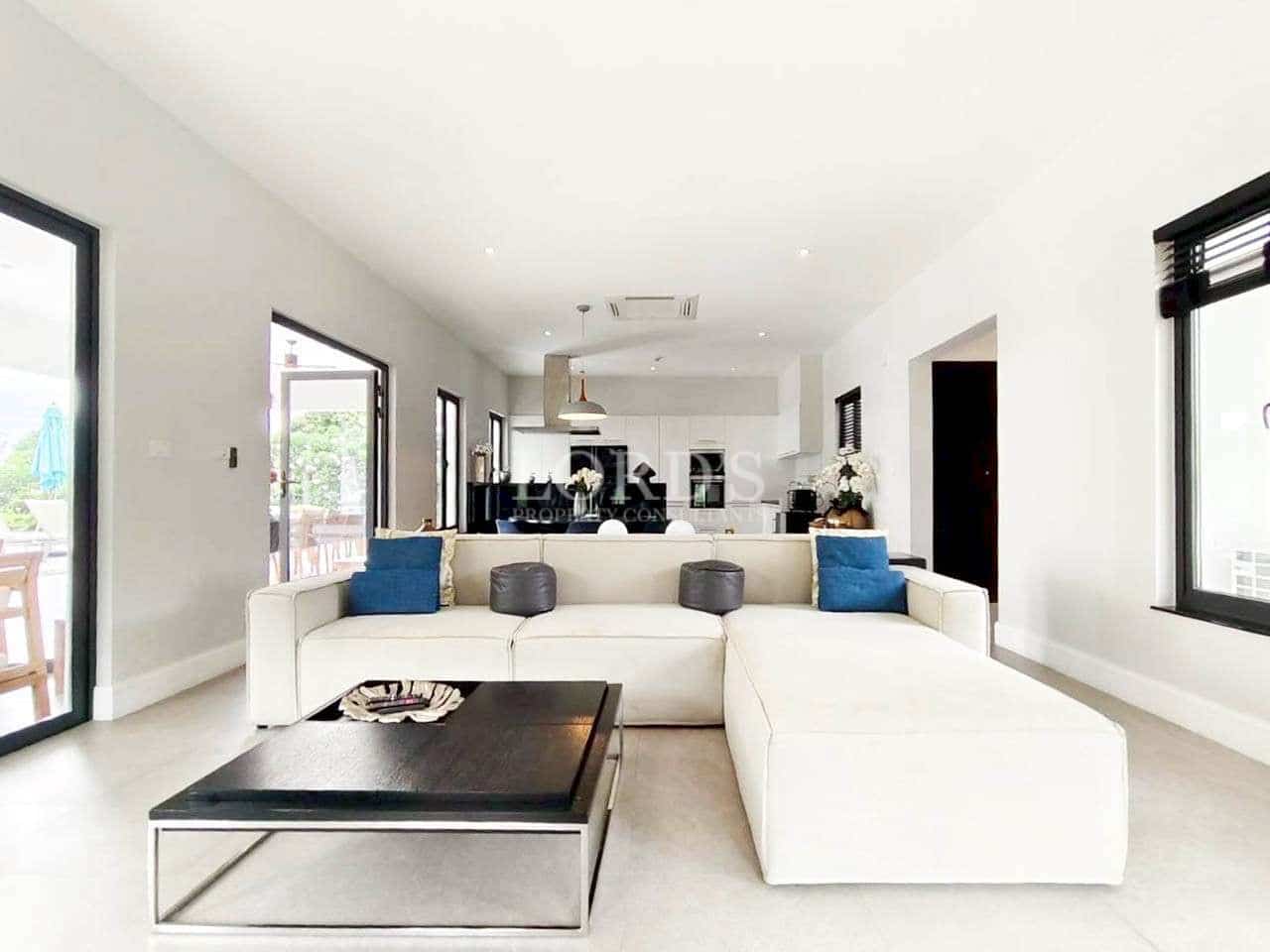 Modern open-plan living room with white sectional sofa, black coffee table, and bright minimalist interior