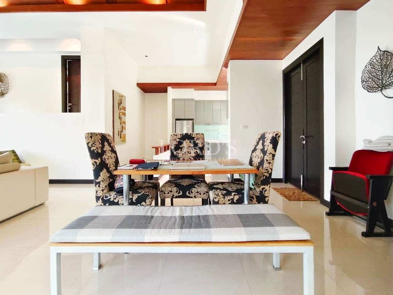 Elegant dining area with patterned chairs, wooden ceiling accents, and open-plan kitchen in a modern luxury villa.