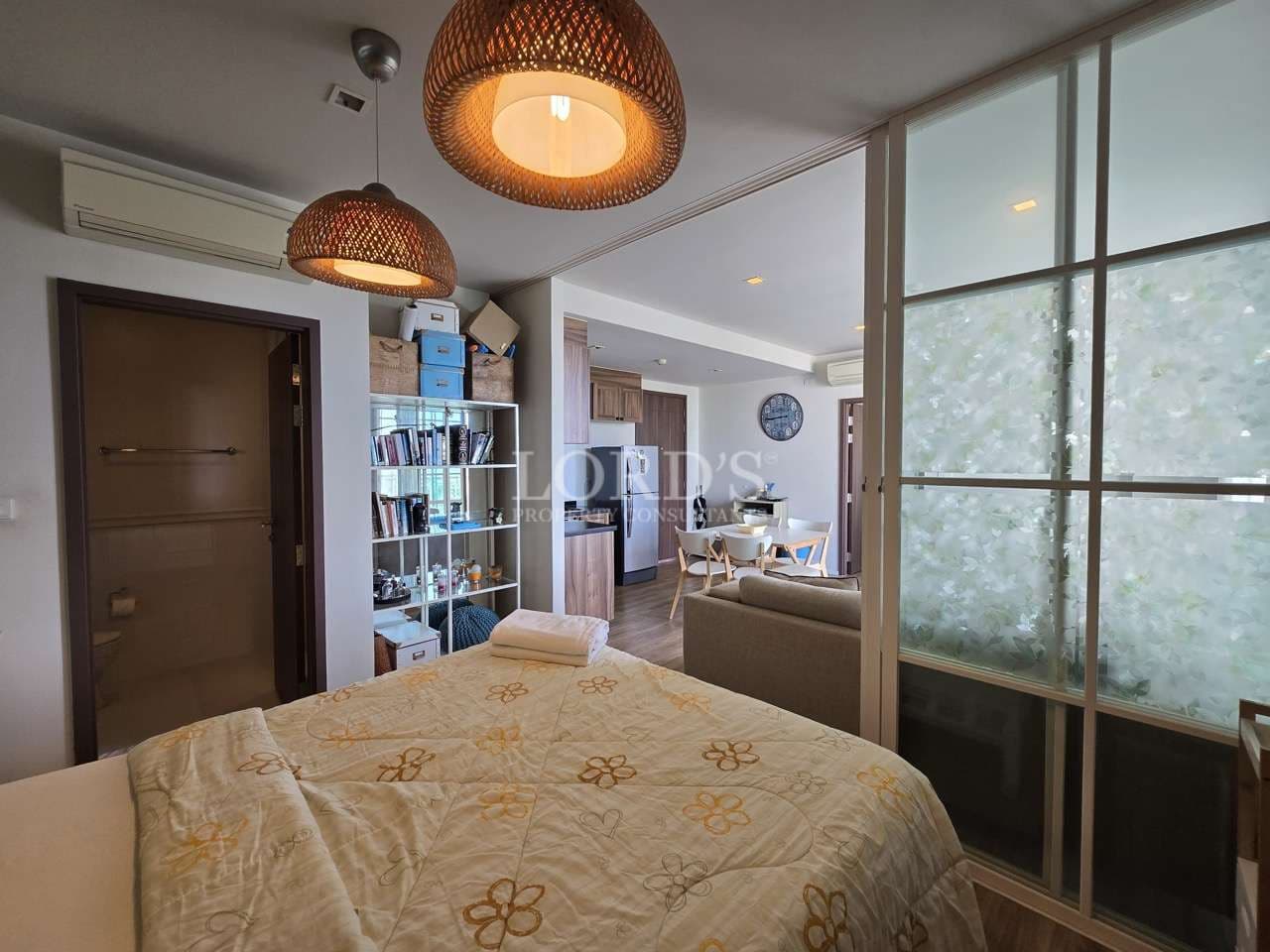 Studio bedroom with double bed, pendant lights, glass partition, and open living area