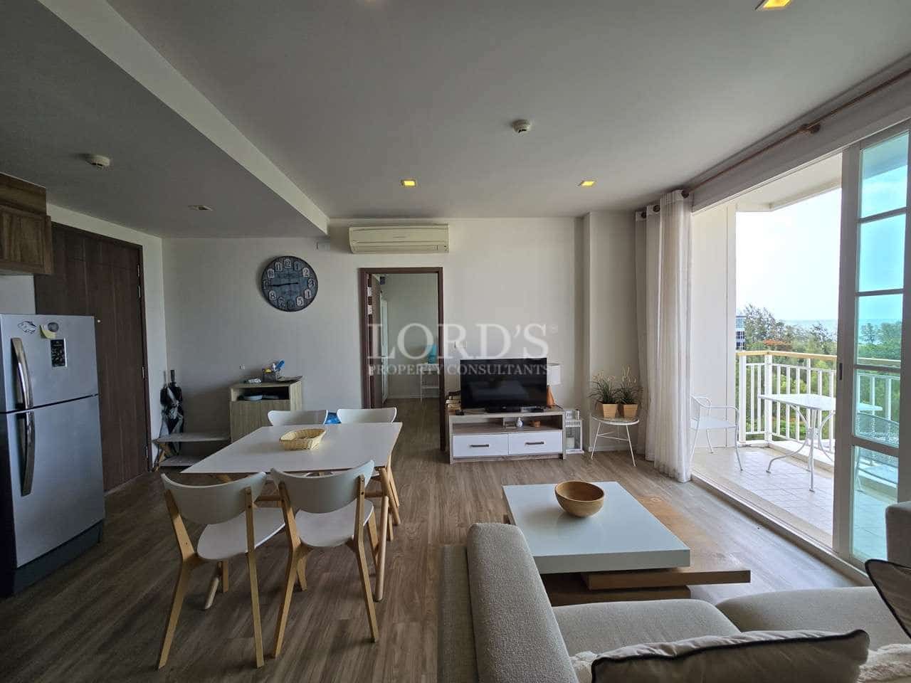 Modern open-plan living room with dining area, kitchen, and balcony access