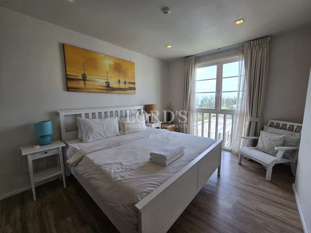 Bright bedroom with white double bed, balcony doors, artwork, and natural light