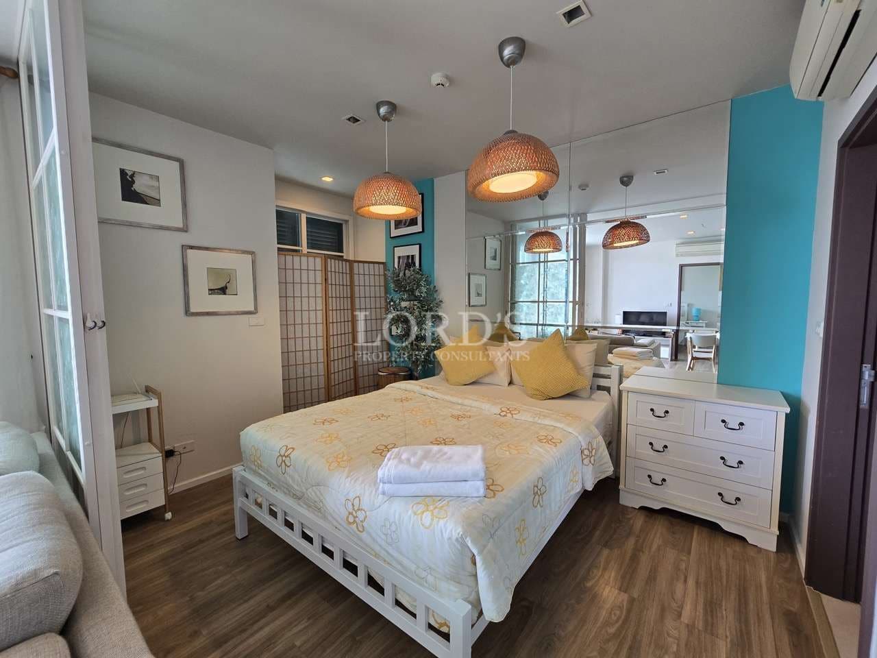 Modern studio bedroom with double bed, pendant lights, mirror wall, and storage drawers