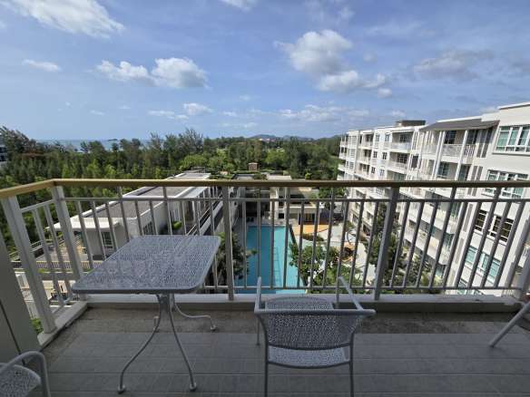 Apartment balcony with outdoor table and chairs overlooking swimming pool and residential buildings
