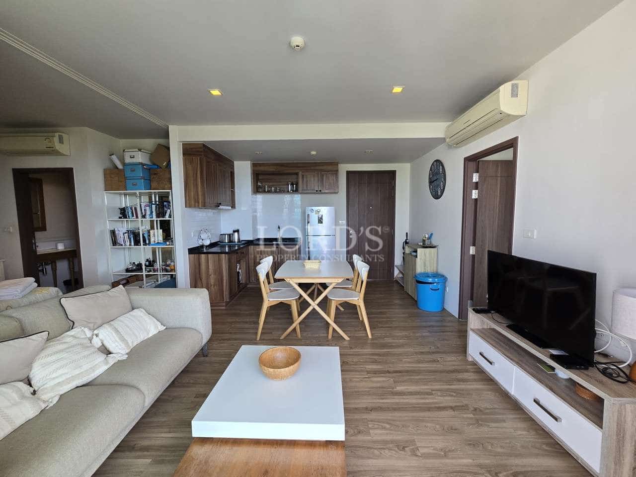 Modern open-plan living room with sofa, dining table, kitchen, and TV unit