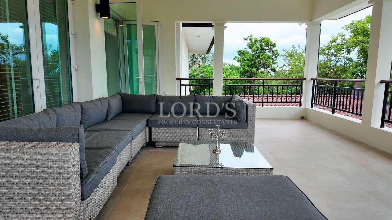 Covered terrace with wicker outdoor sofa, glass coffee table, and garden views in a luxury villa.