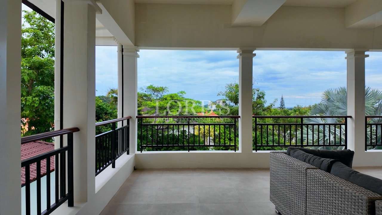 Spacious covered balcony with modern railings, outdoor seating, and lush green garden views.