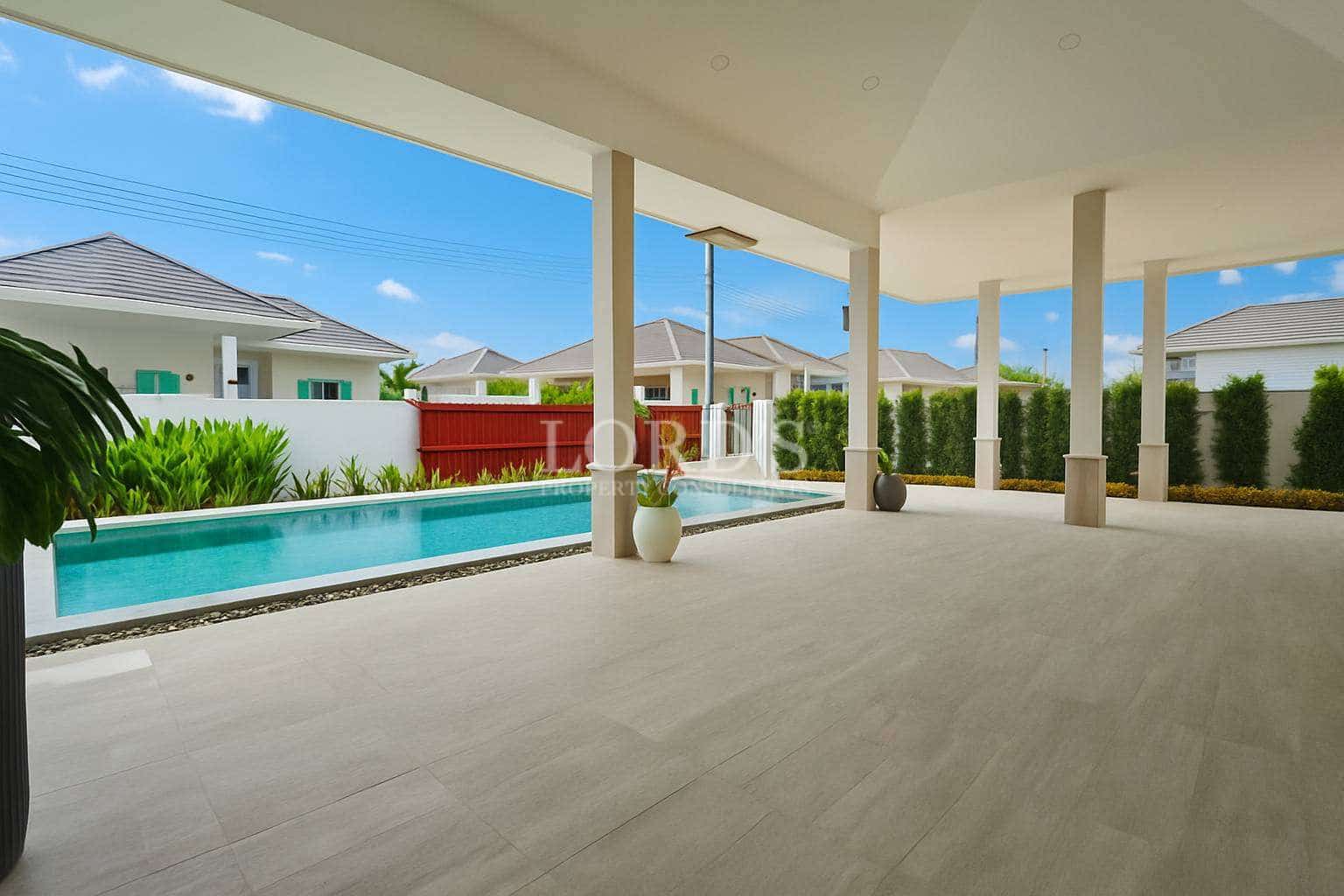 Spacious covered outdoor terrace overlooking a private swimming pool with landscaped greenery and neighboring villas.