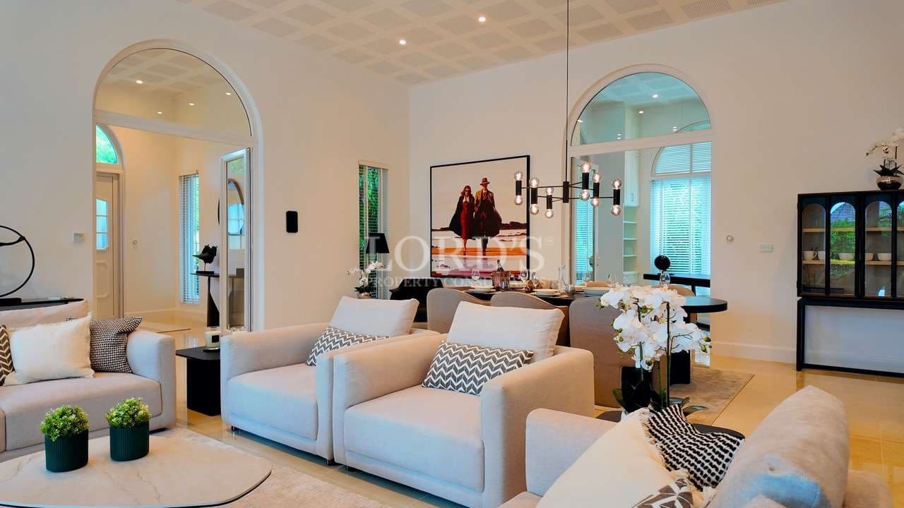 Luxury open-plan living and dining area with modern sofas, arched windows, and elegant chandelier.