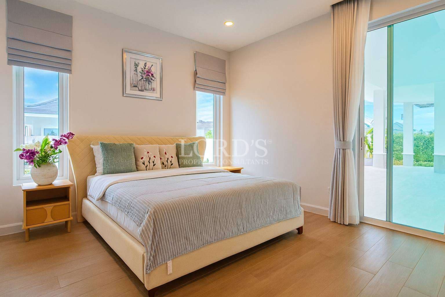 Bright modern bedroom with upholstered bed, wooden flooring, large sliding glass door, and outdoor terrace view.