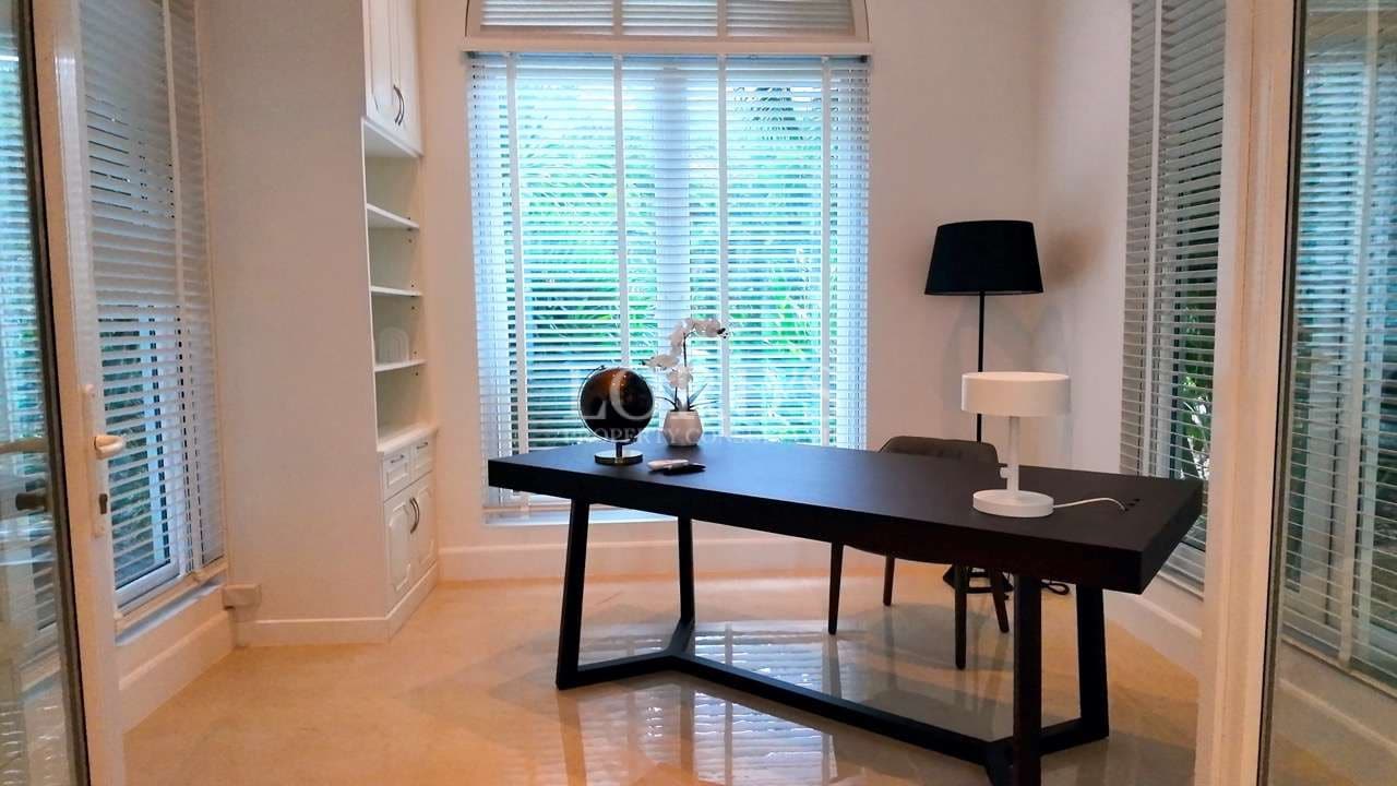 Modern home office with black desk, large windows, white blinds, and minimalist interior design.