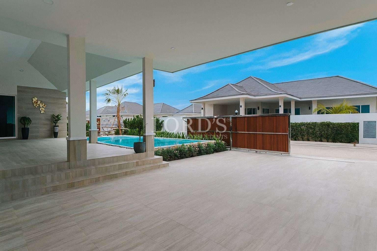 Modern villa entrance with covered patio, private swimming pool, tiled driveway, and wooden sliding gate.