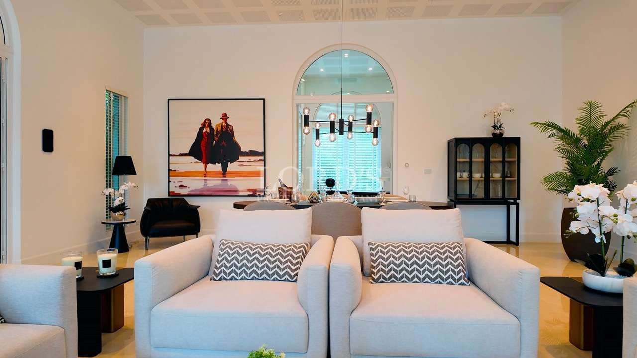 Modern luxury living room with beige sofas, arched window, chandelier, and elegant dining area.