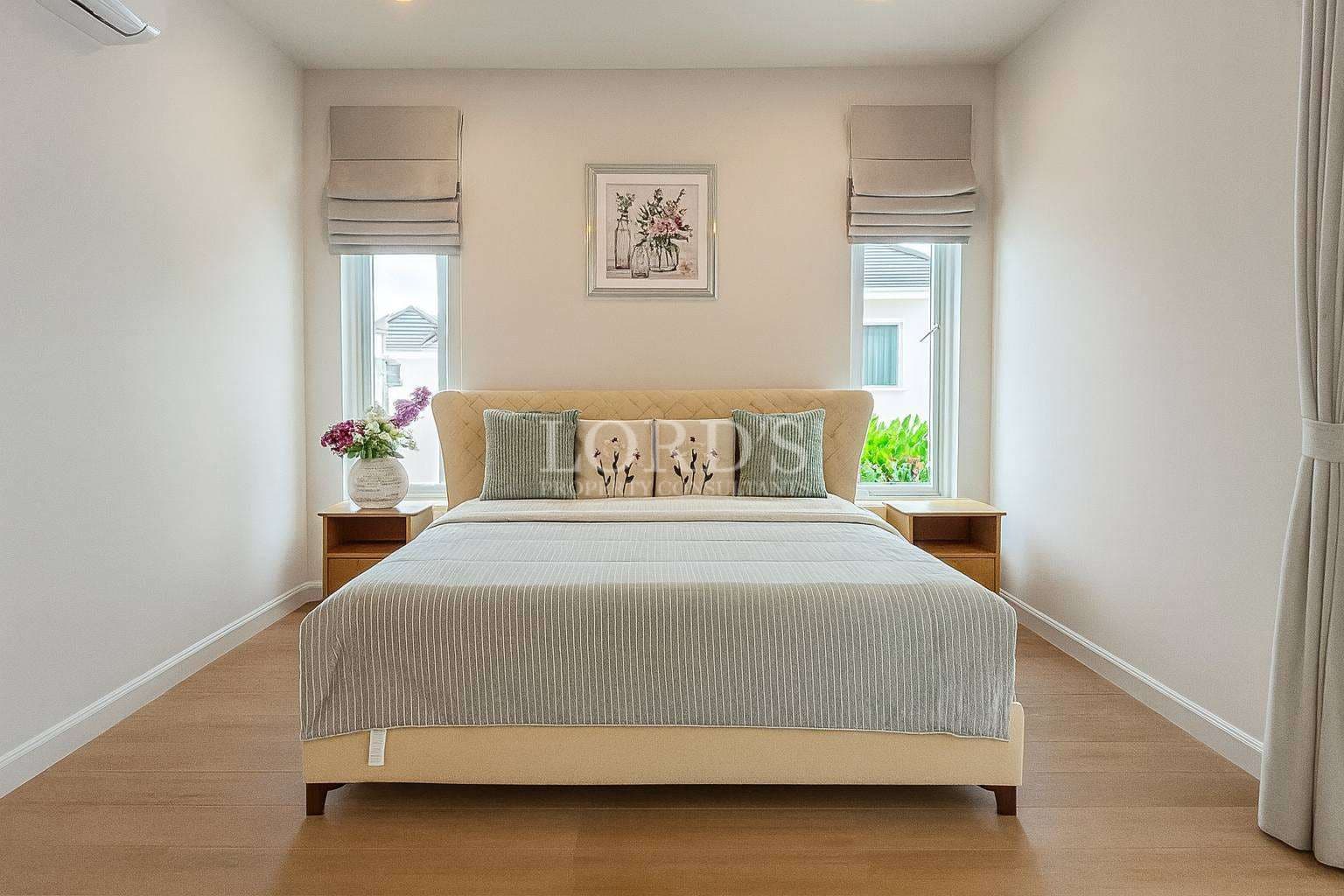 Elegant neutral bedroom with upholstered bed, wooden flooring, twin windows, and soft natural light