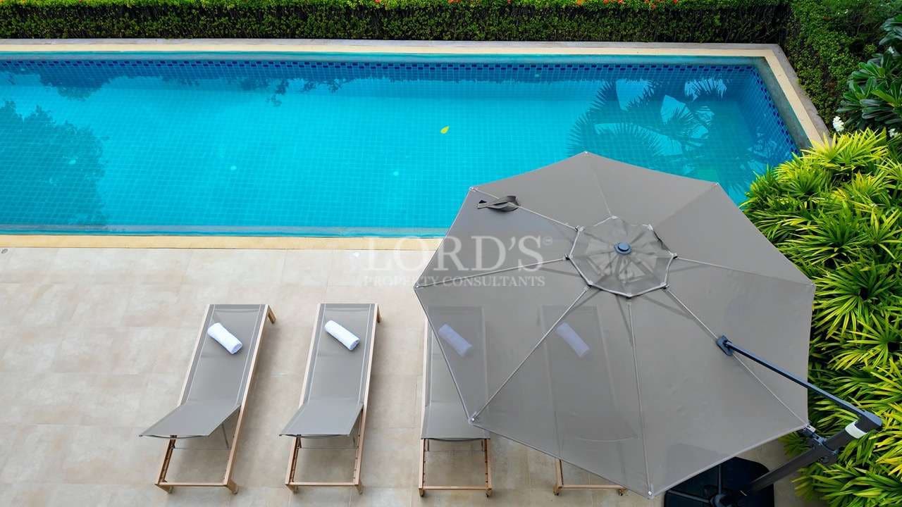 Aerial view of luxury swimming pool with sun loungers and large patio umbrella in a private villa.
