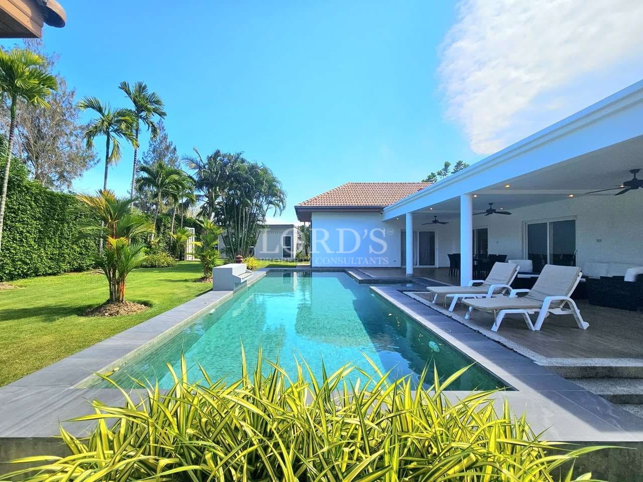 Luxury private swimming pool with sun loungers, covered terrace, tropical garden, and modern villa architecture.