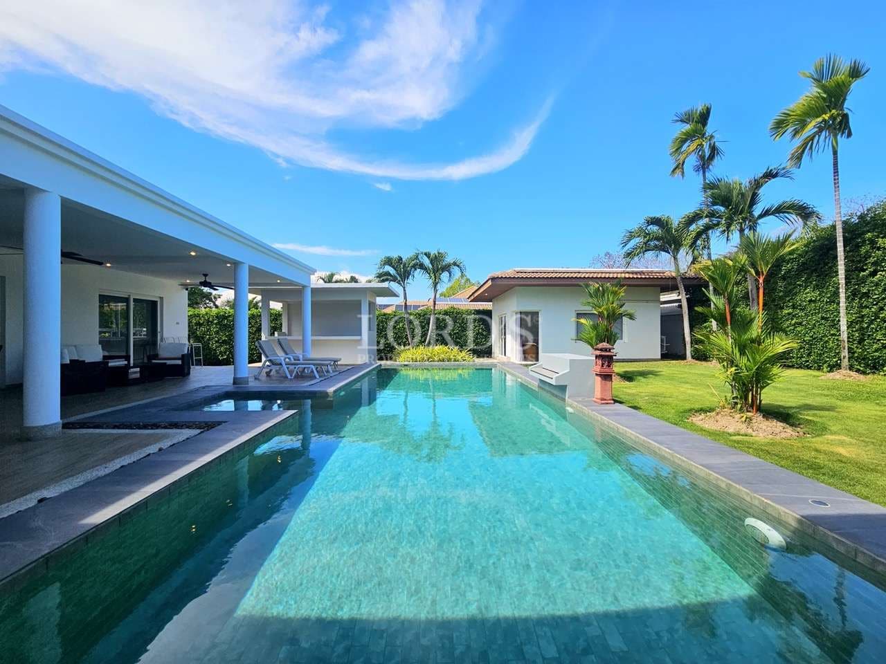 Luxury tropical villa with private swimming pool, palm trees, and modern outdoor seating under a clear blue sky.