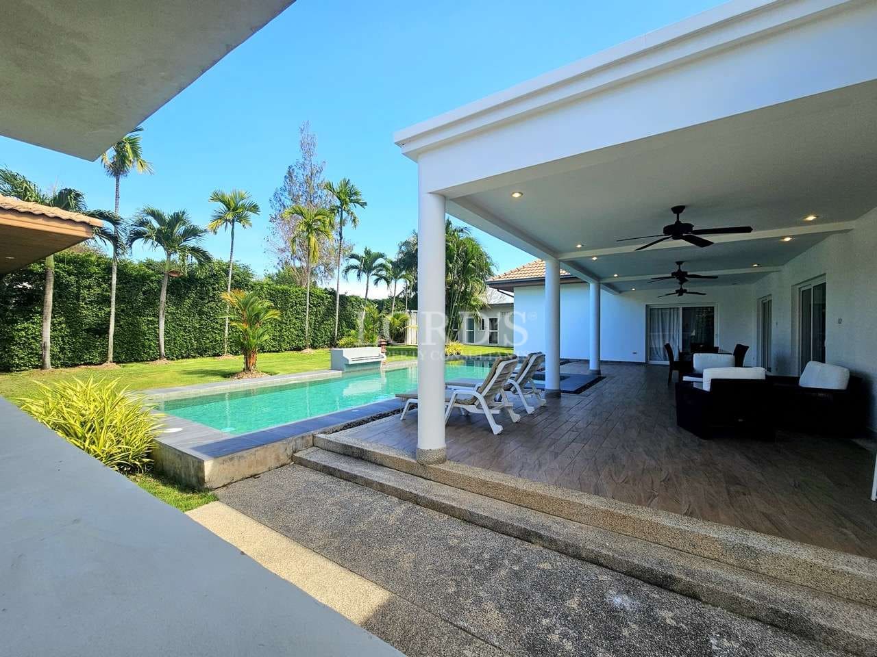 Luxury poolside terrace with sun loungers, covered outdoor seating, ceiling fans, and landscaped tropical garden.