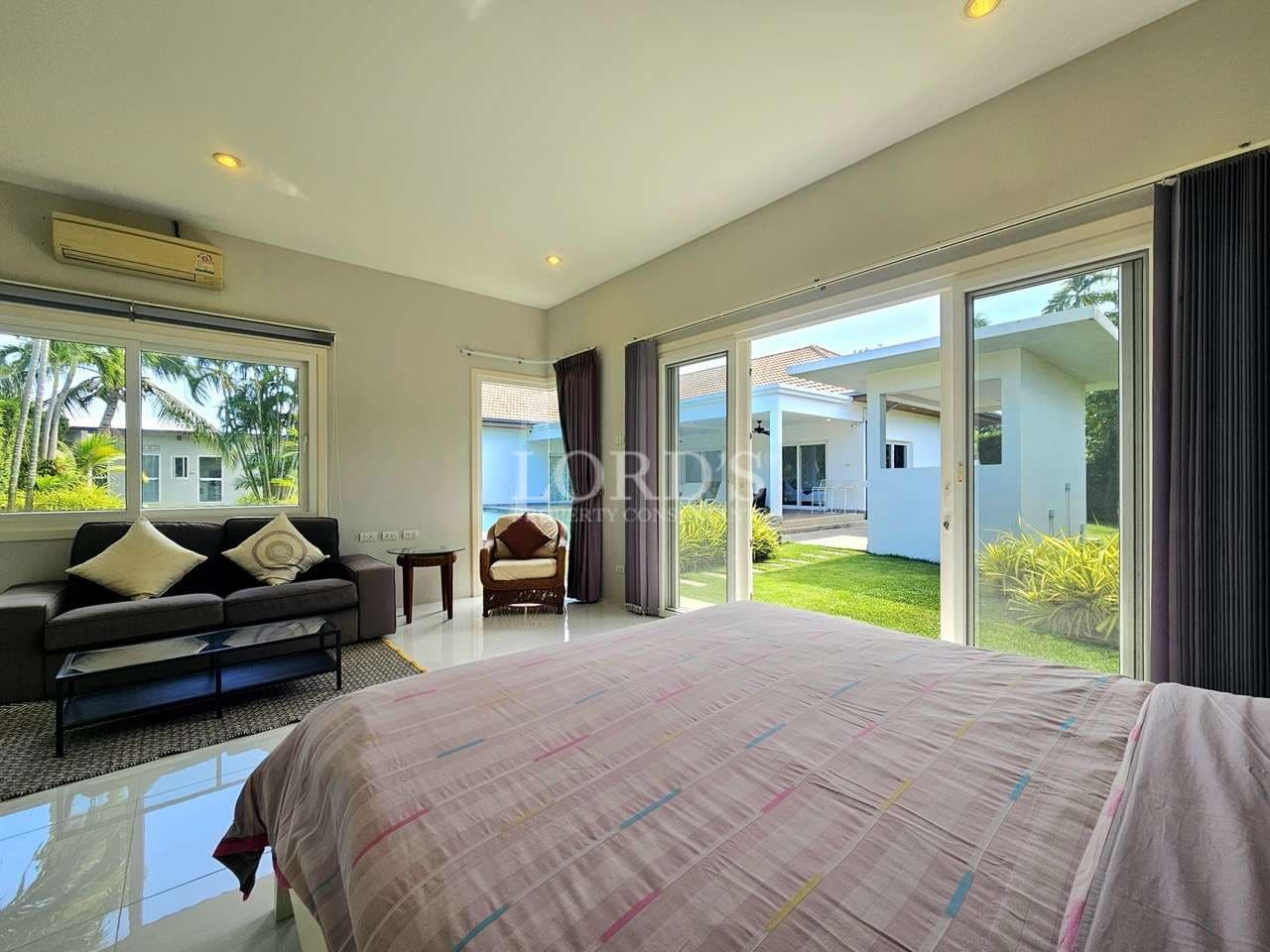 Bright modern bedroom with sliding glass doors, garden view, sofa seating, and natural daylight.