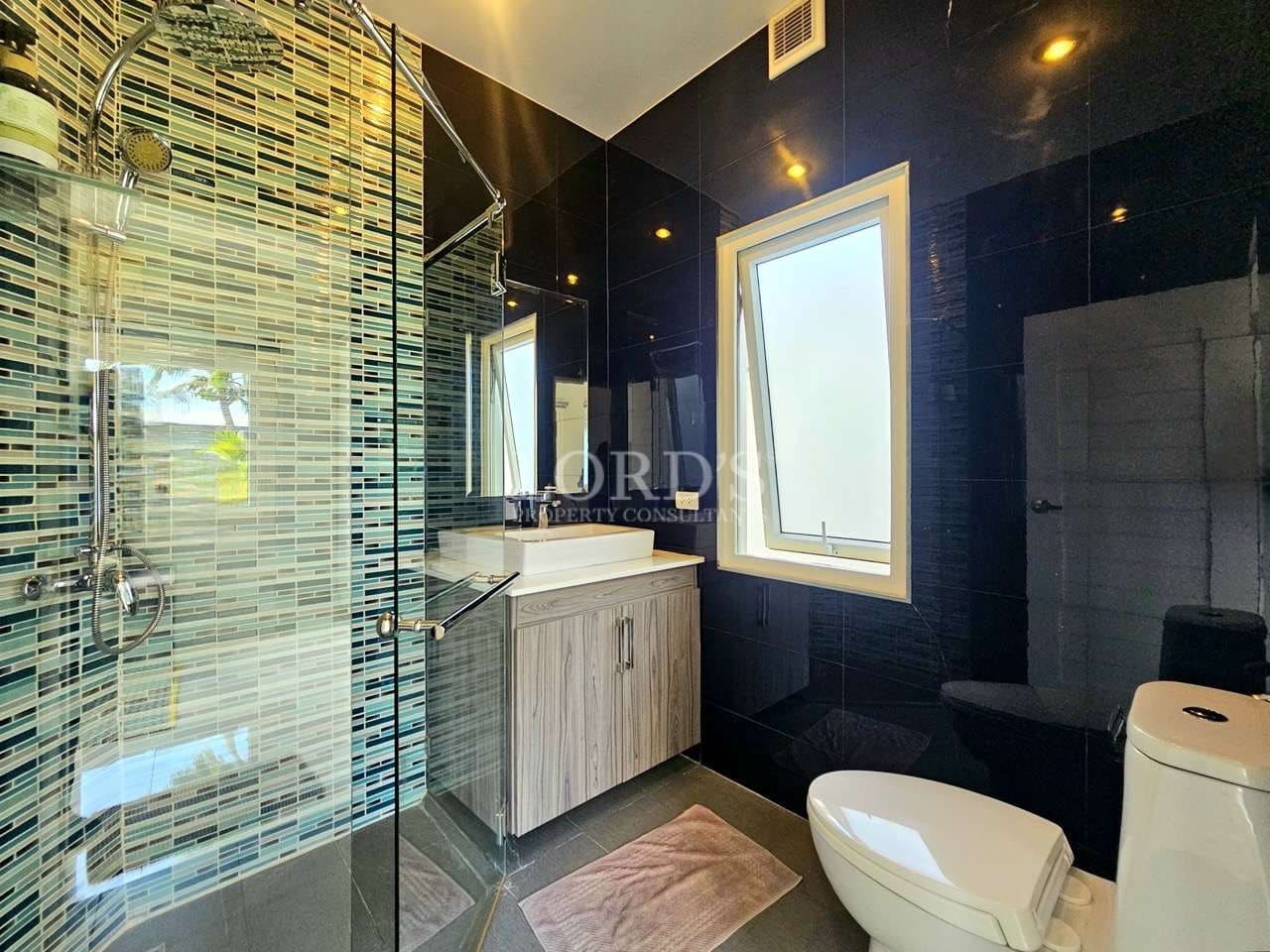 Modern bathroom with glass shower, mosaic tile wall, black glossy tiles, vanity sink, and toilet.