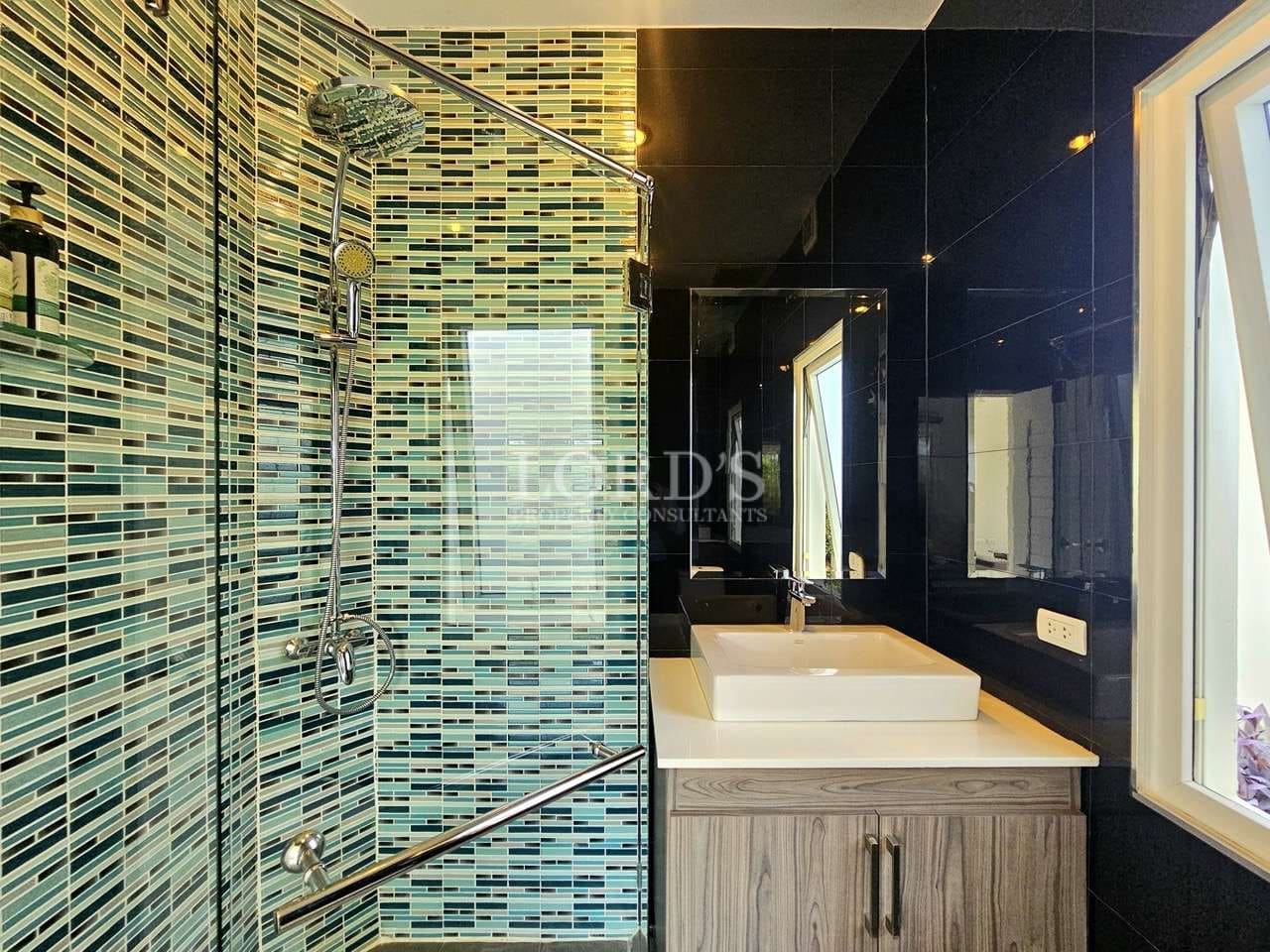 Modern bathroom with glass-enclosed shower, mosaic tile accent wall, rainfall showerhead, and sleek vanity sink.