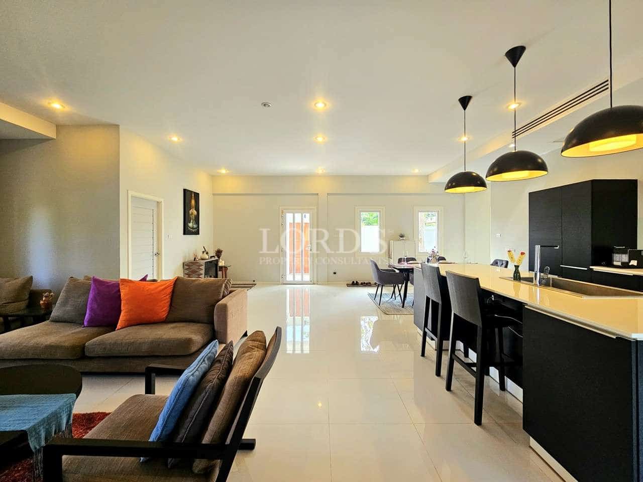 Modern open-plan living room with kitchen island, bar stools, pendant lighting, and contemporary furniture.