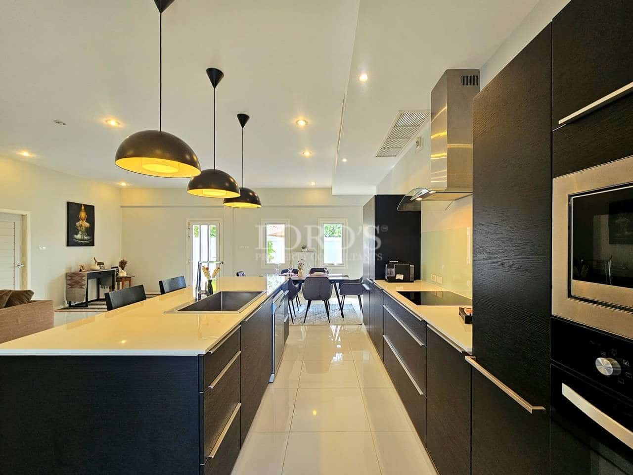 Modern open-plan kitchen with double island counters, black cabinetry, pendant lighting, and dining area in the background.