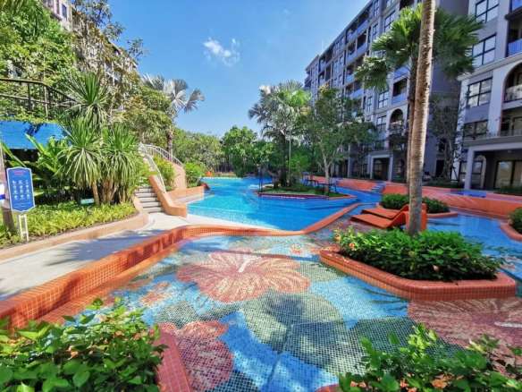 Luxury condominium lagoon-style swimming pool with mosaic tiles, tropical landscaping, palm trees, and modern apartment buildings.