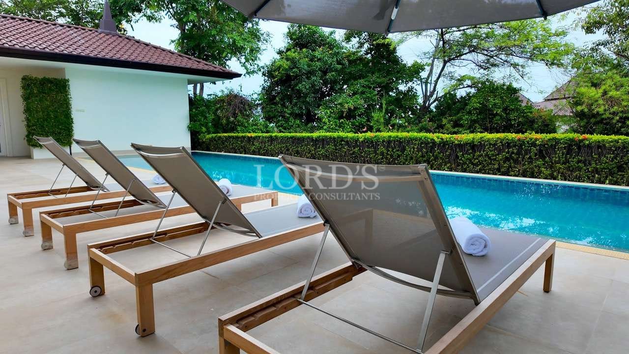 Luxury private swimming pool with sun loungers and umbrellas in a tropical villa setting.