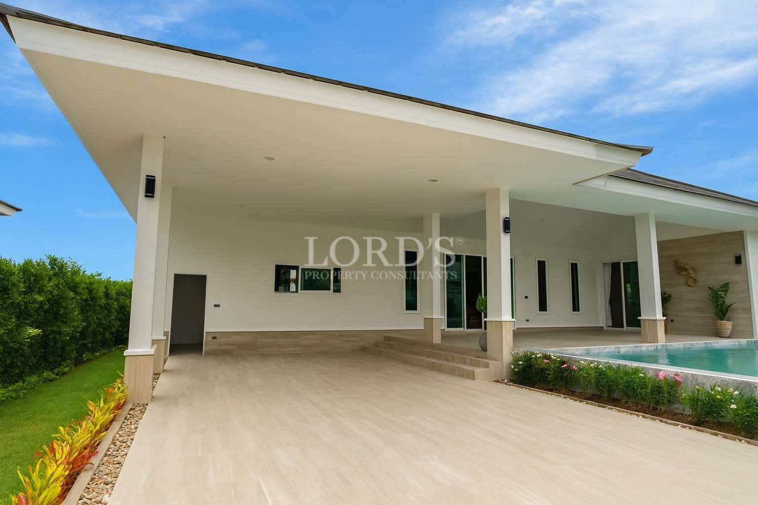 Modern luxury villa exterior with covered carport, private swimming pool, white facade, and landscaped garden.
