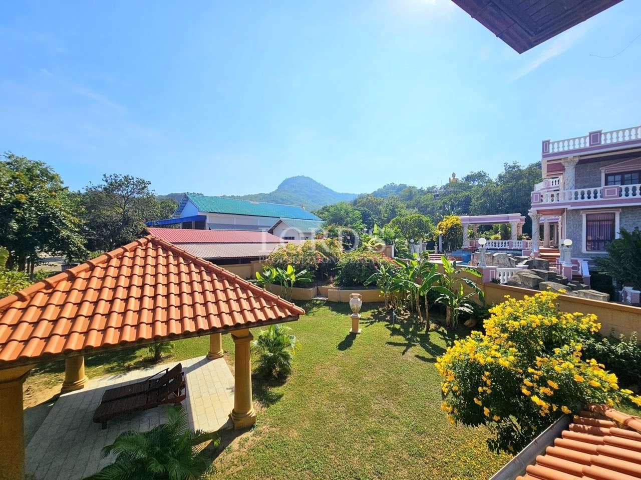 Elevated garden view with landscaped lawn, pavilion seating area, tropical plants, and mountain backdrop.