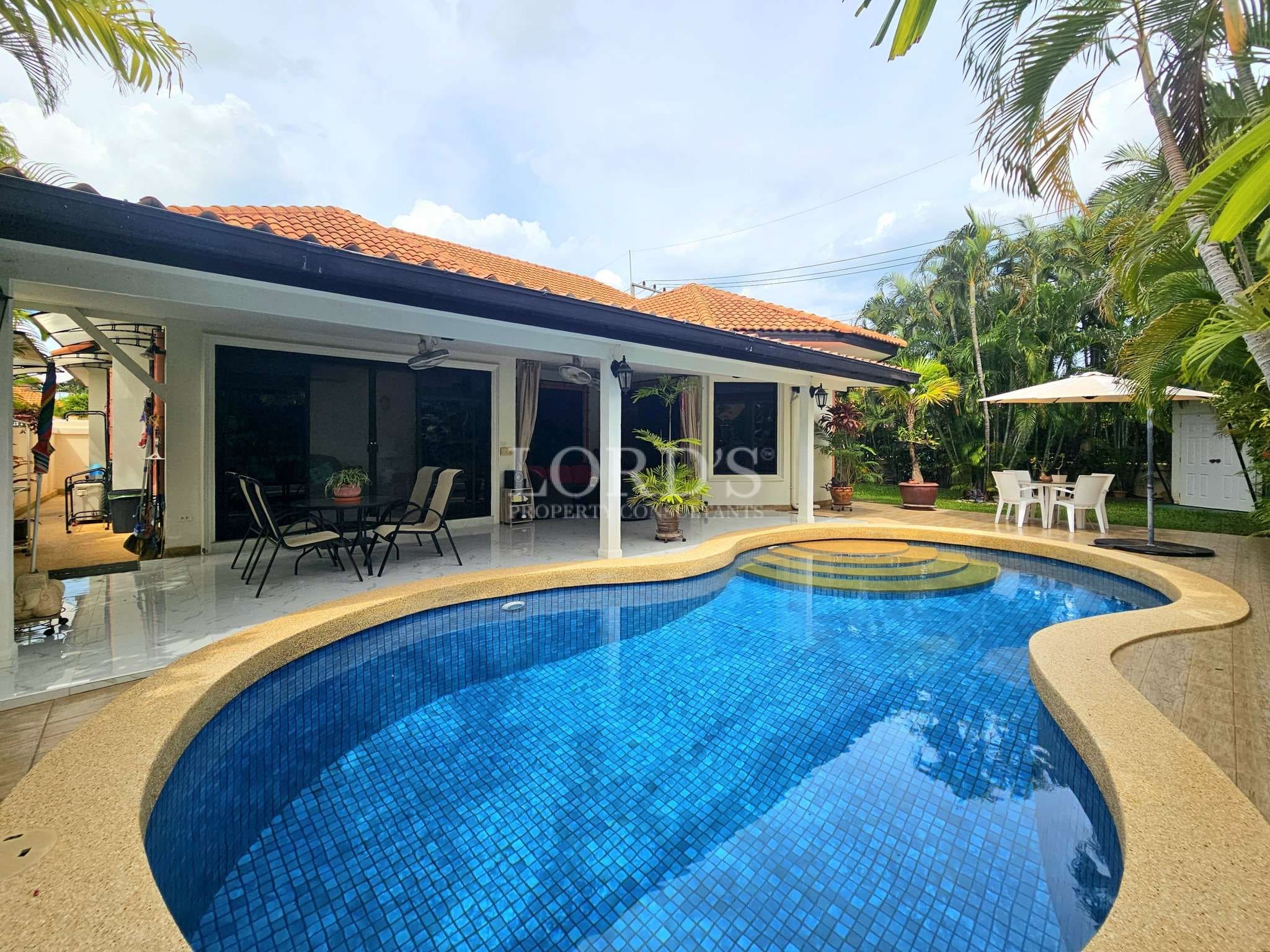 Private swimming pool with curved design, poolside patio seating, and tropical villa exterior