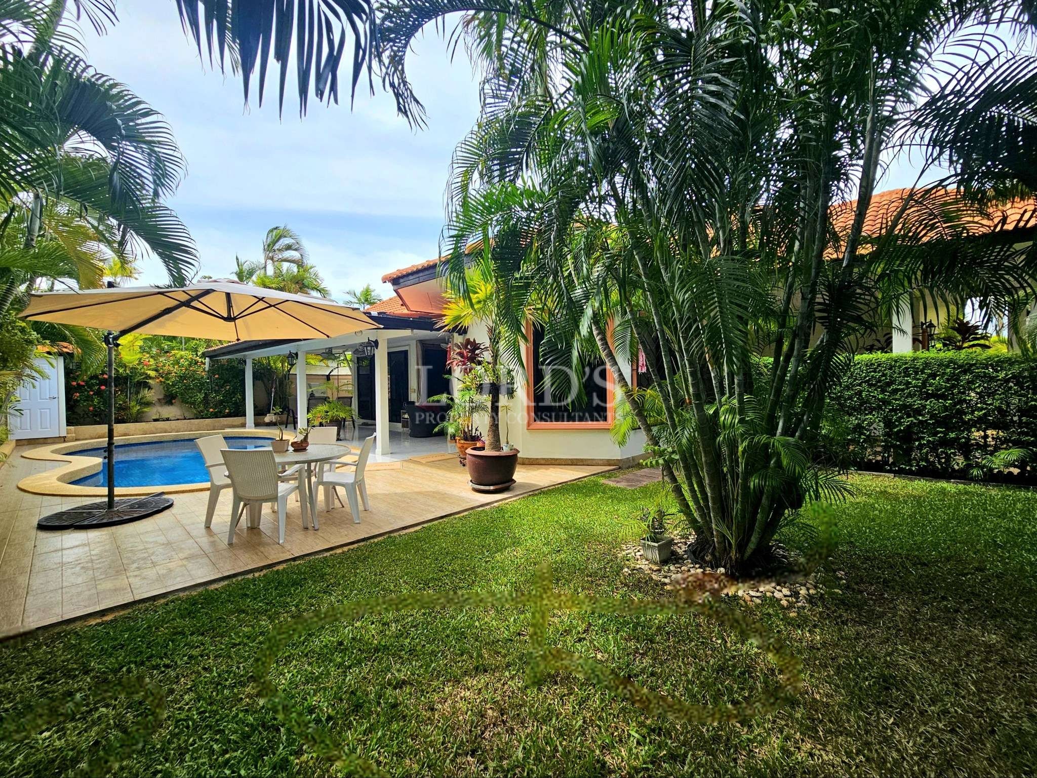 Tropical backyard with swimming pool, outdoor dining area, umbrella seating, and lush green garden