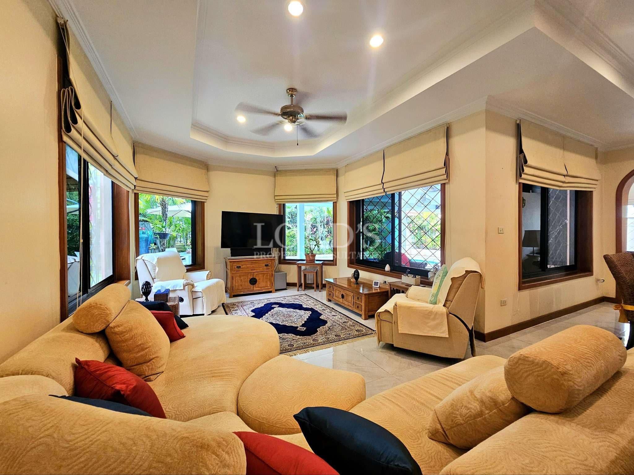 Spacious living room with beige sofas, large windows, recessed ceiling lighting, and garden views
