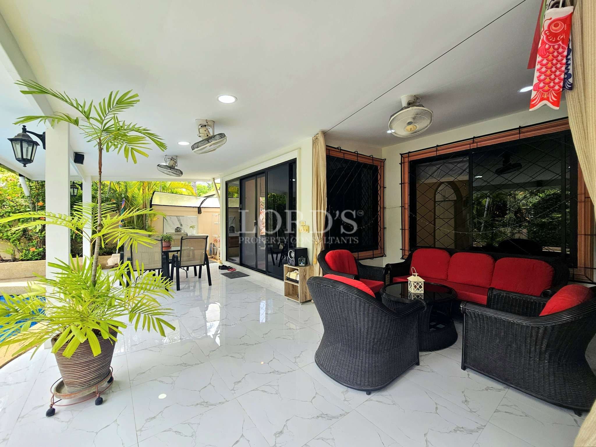 Covered outdoor patio with seating area, tiled flooring, ceiling fans, and garden views.