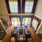 Luxury double-height living room with classic interior design, tall windows, elegant draped curtains, symmetrical sofa seating, and natural light-filled space.