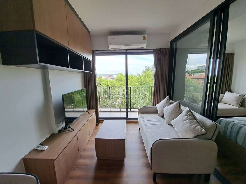 Modern living room with sofa, TV unit, sliding glass partition, and balcony view overlooking green trees.