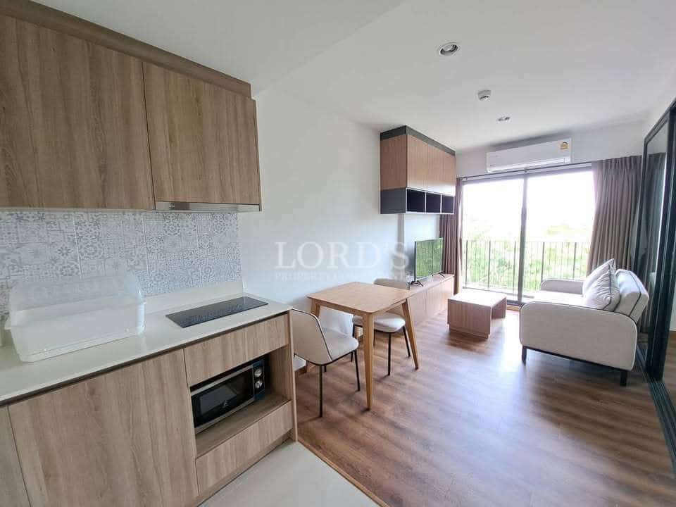 Modern studio apartment interior with compact kitchen, dining table, sofa, TV unit, and large balcony window.