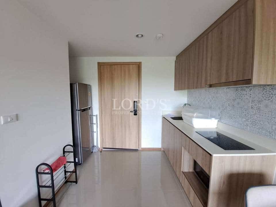 Modern compact kitchenette with wooden cabinets, built-in electric cooktop, patterned backsplash, refrigerator, and minimalist interior design.