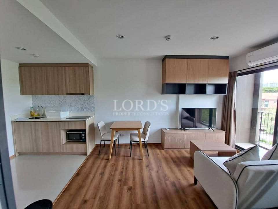 Modern studio apartment interior with open kitchenette, dining area, wooden flooring, built-in TV unit, and balcony access.