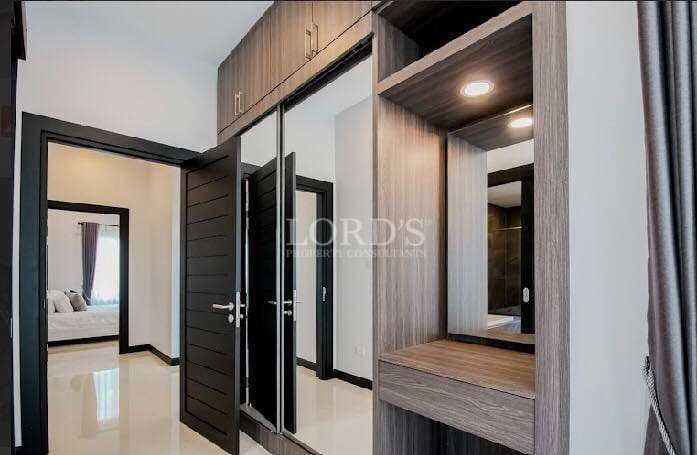 Modern dressing area with built-in wardrobe, vanity seating, mirror lighting, and adjacent bedroom access.