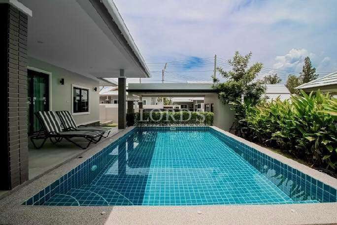 Private swimming pool beside modern villa with sun loungers, tiled deck, and landscaped greenery.
