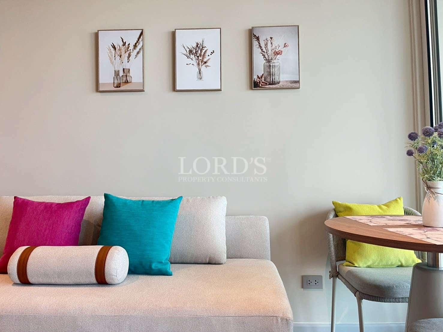 Modern studio living area with sofa, colorful cushions, wall art, and dining corner.