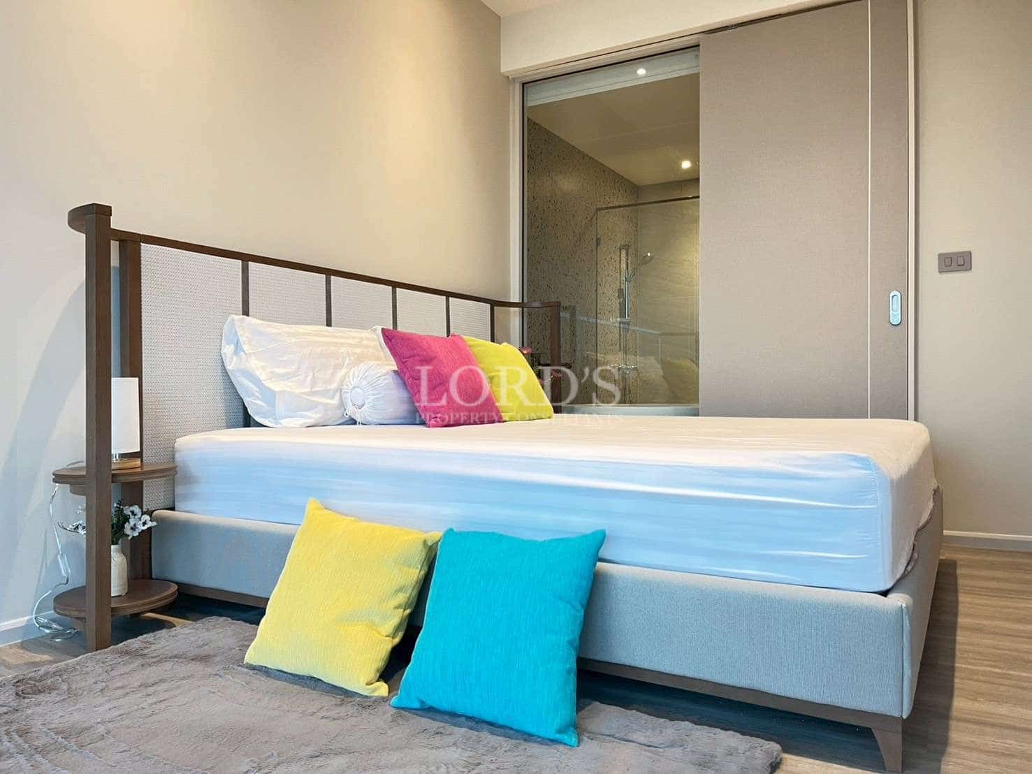 Modern bedroom with low-profile bed, colorful cushions, and ensuite bathroom access.