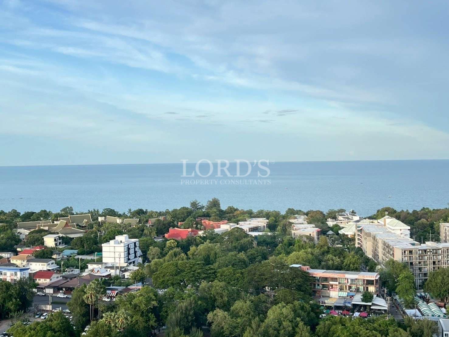 Panoramic coastal view overlooking residential buildings, greenery, and the open sea.