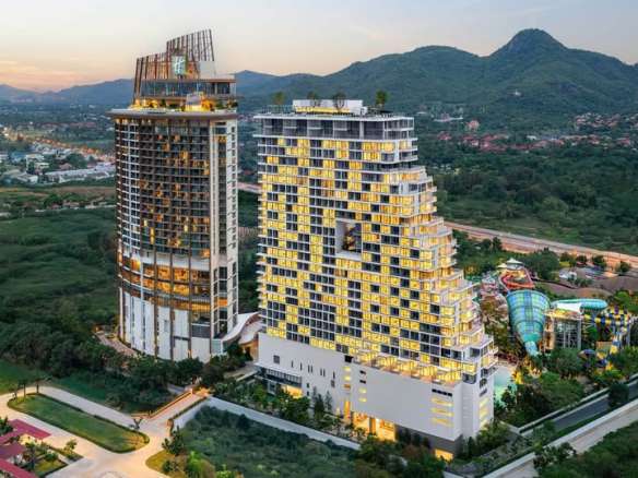 Luftaufnahme eines modernen Luxuswohnkomplexes mit Hochhaustürmen und Berglandschaft bei Sonnenuntergang.