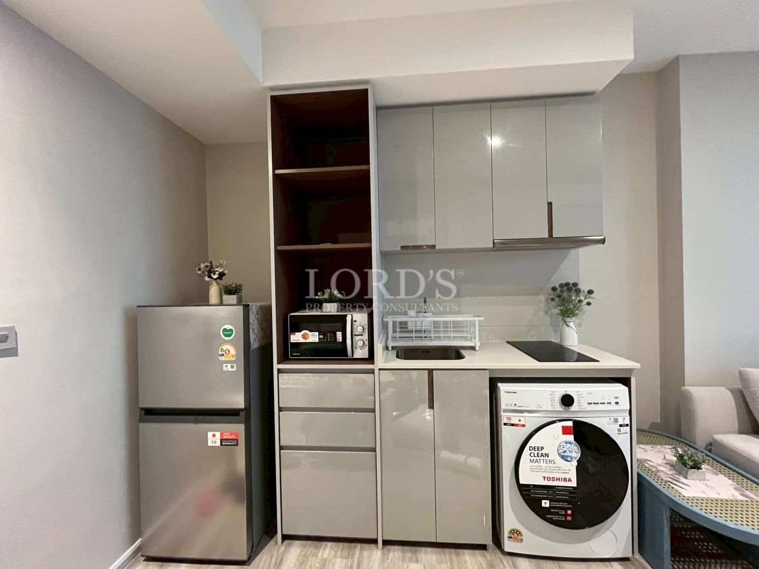 Compact modern kitchenette with refrigerator, washer, built-in cabinets, and cooking area.